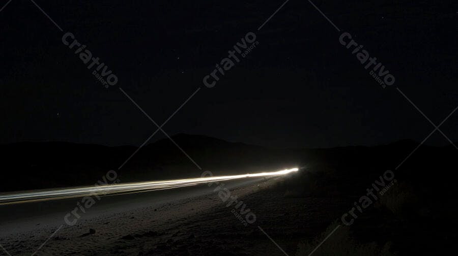 Rastros de luz de carro em estrada rural à noite com montanhas distantes