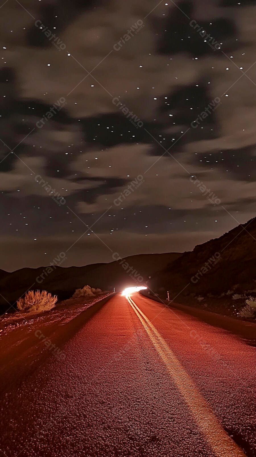 Estrada deserta à noite com luzes de carro, céu estrelado e montanhas distantes