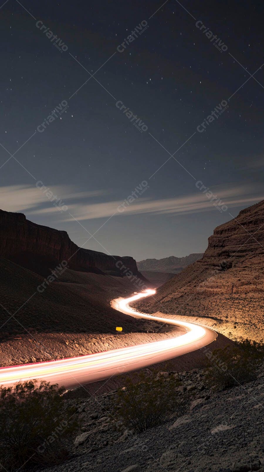 Estrada sinuosa com rastros de luz à noite em cânion desértico sob céu estrelado