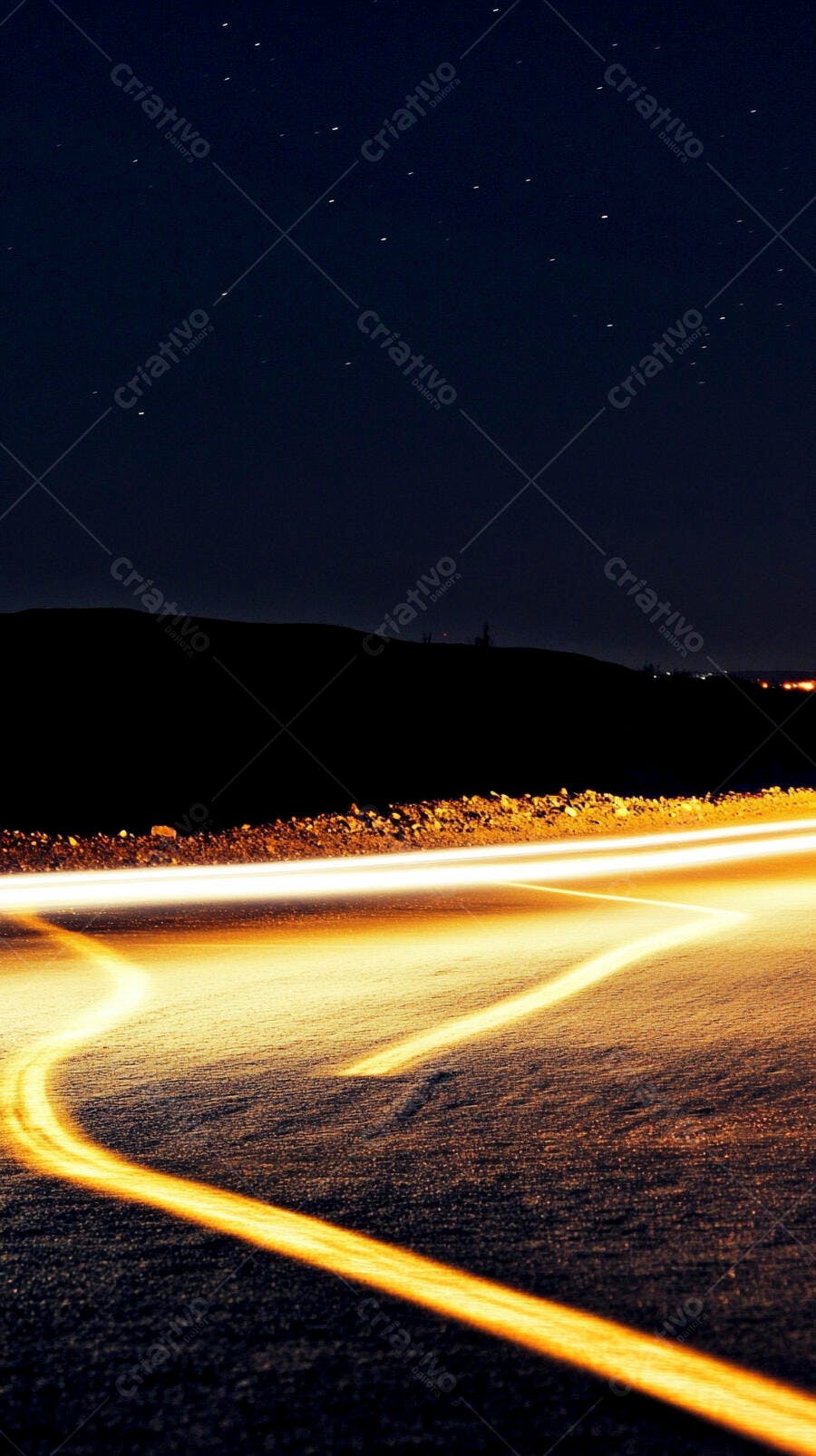 Rastros de luz laranja em estrada noturna sob céu estrelado