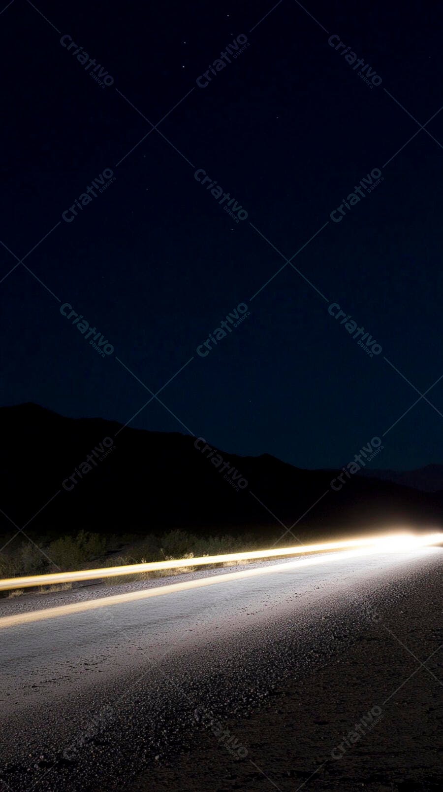 Estrada noturna com rastros de luz de carro e montanhas sob céu estrelado
