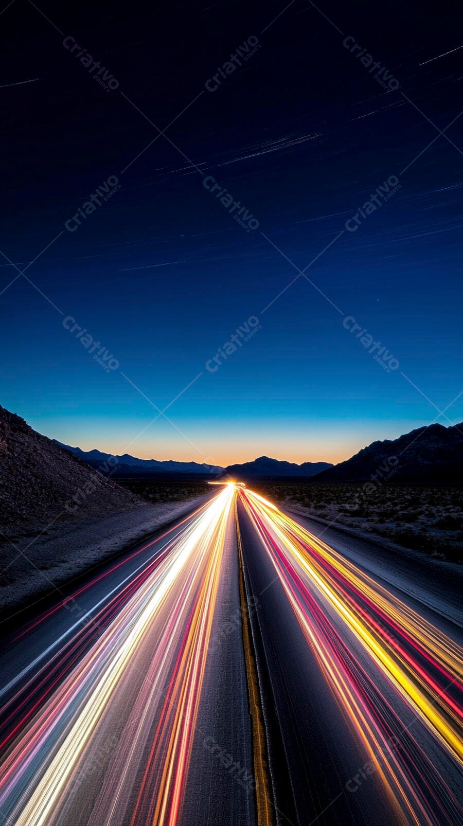 Rodovia deserta com trilhas de luzes de carros ao entardecer entre montanhas