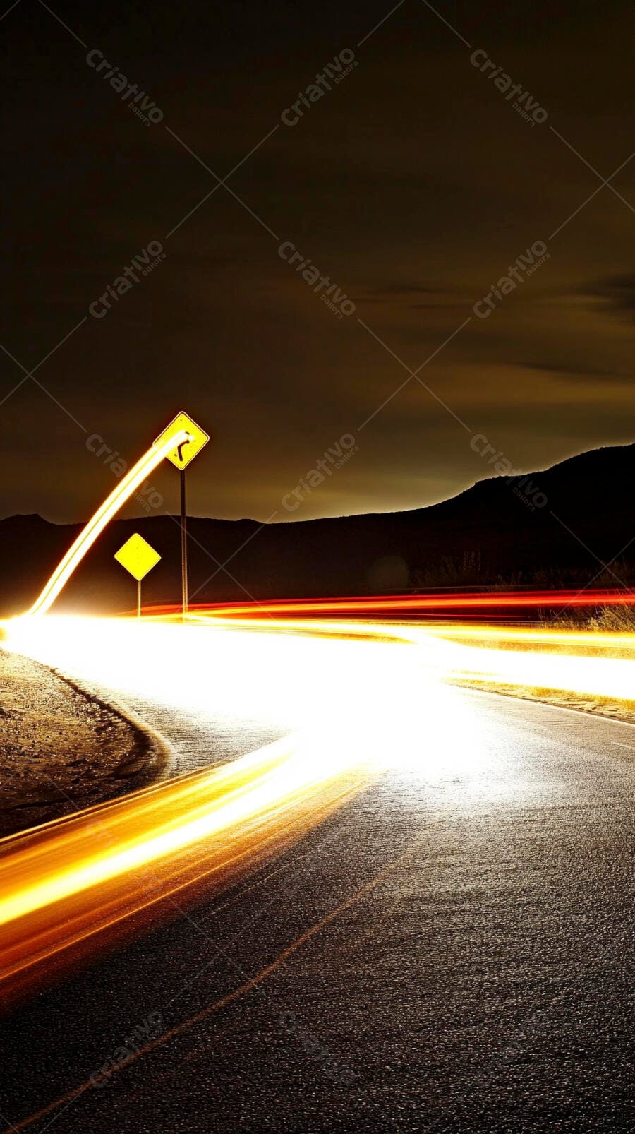 Trilhas de luz laranja e branca em estrada noturna com placas de curva