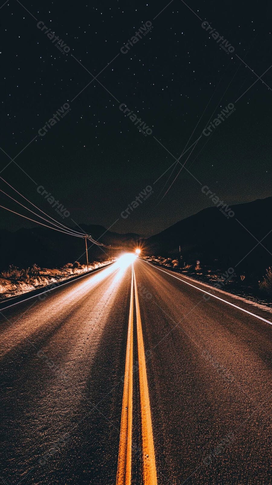 Rodovia à noite com faróis distantes sob céu estrelado e montanhas