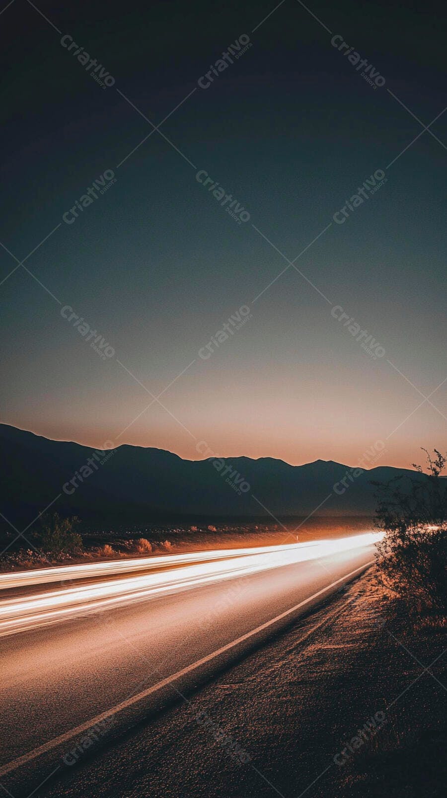 Rodovia com rastros de luz ao pôr do sol entre montanhas
