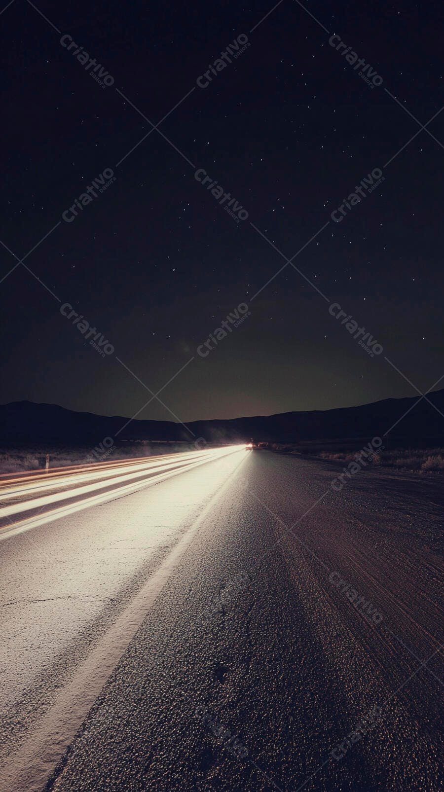 Rodovia noturna com rastros de luz de carro e céu estrelado sobre montanhas