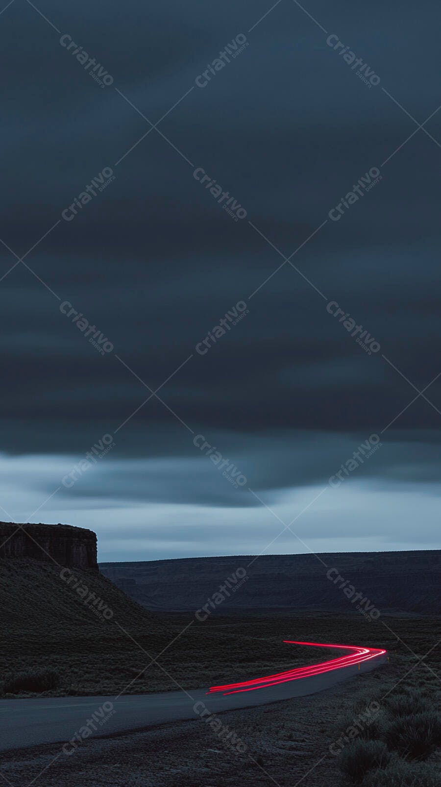 Estrada rural noturna com rastros de luz vermelha e montanhas distantes