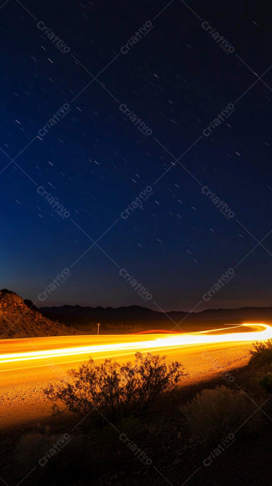 Estrada noturna com rastros de luz e céus estrelados sobre montanhas no deserto