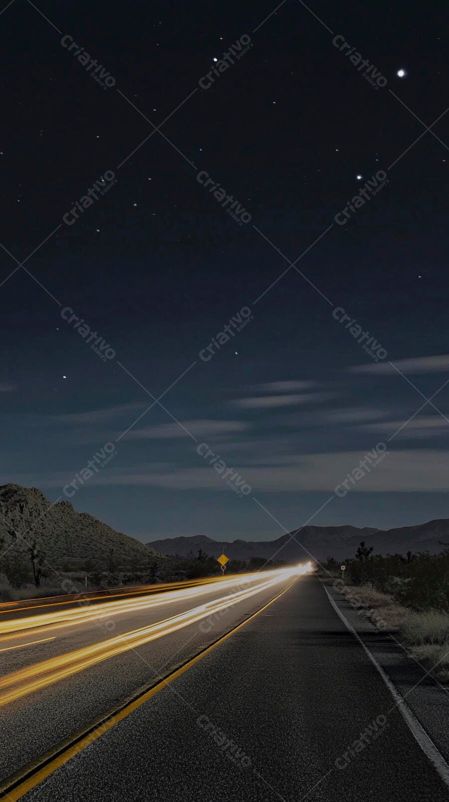Estrada noturna com rastros de luz e céu estrelado sobre montanhas áridas