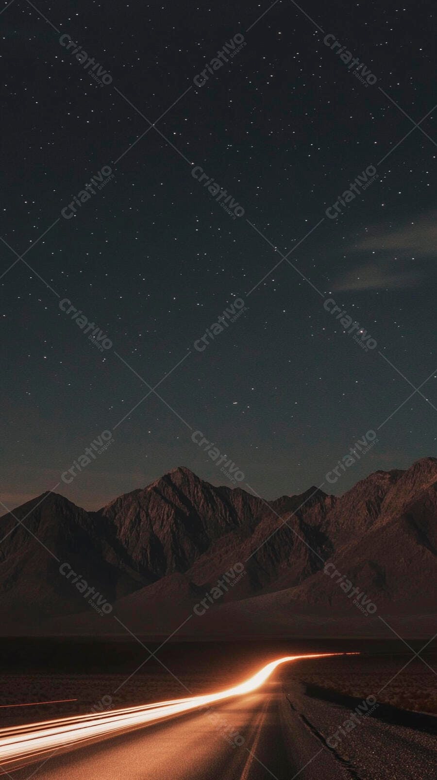 Estrada noturna entre montanhas sob céu estrelado com rastros de luz de veículos