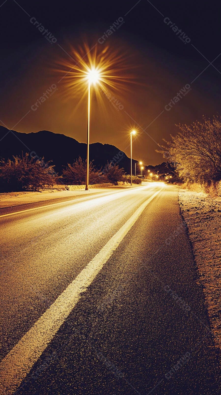 Estrada noturna iluminada entre montanhas áridas com postes de luz
