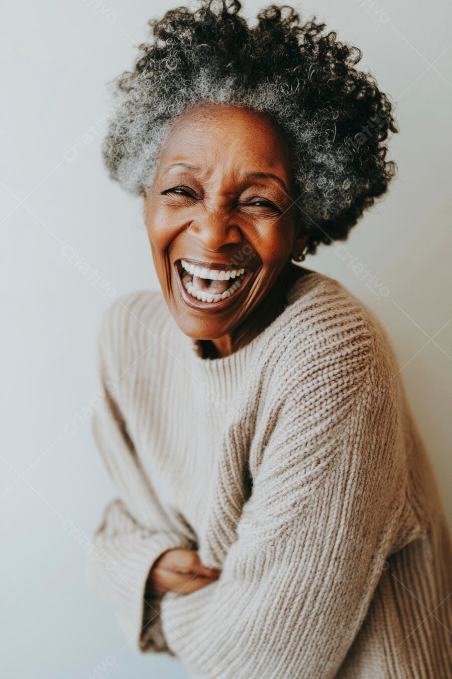 Mulher idosa negra rindo alegremente com cabelo grisalho crespo e suéter bege