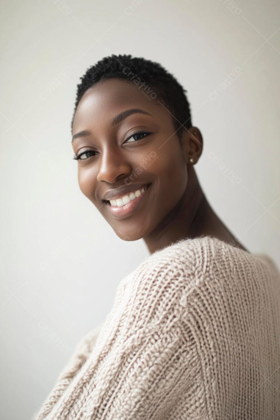 Mulher negra jovem sorrindo com cabelo curto e suéter bege em fundo claro