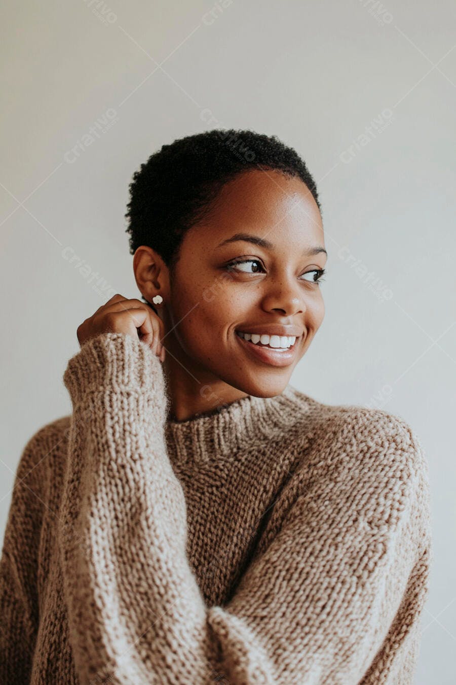 Mulher negra sorrindo de cabelo curto e suéter bege em plano de fundo claro