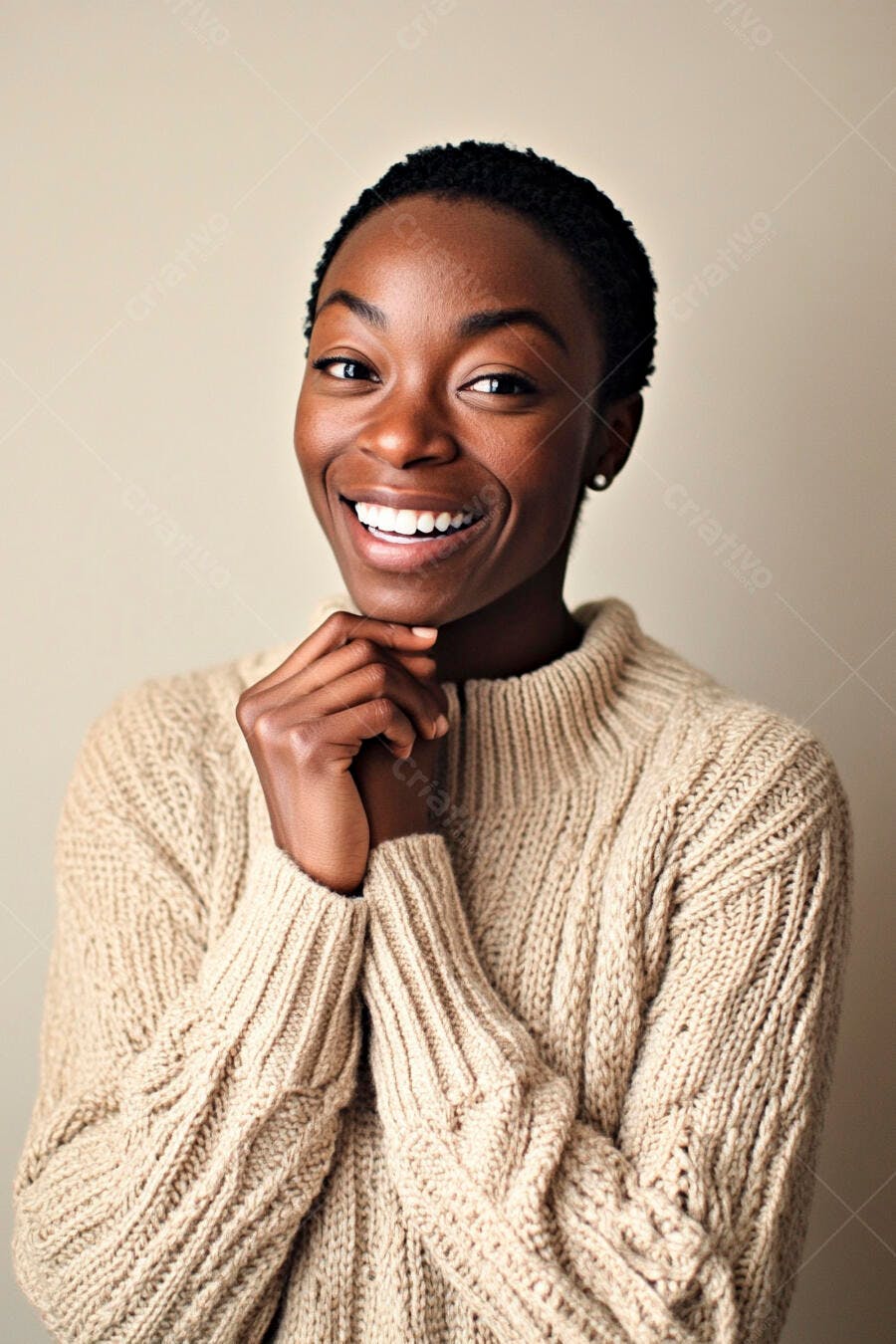 Mulher negra sorrindo com suéter bege tricotado e mãos no queixo