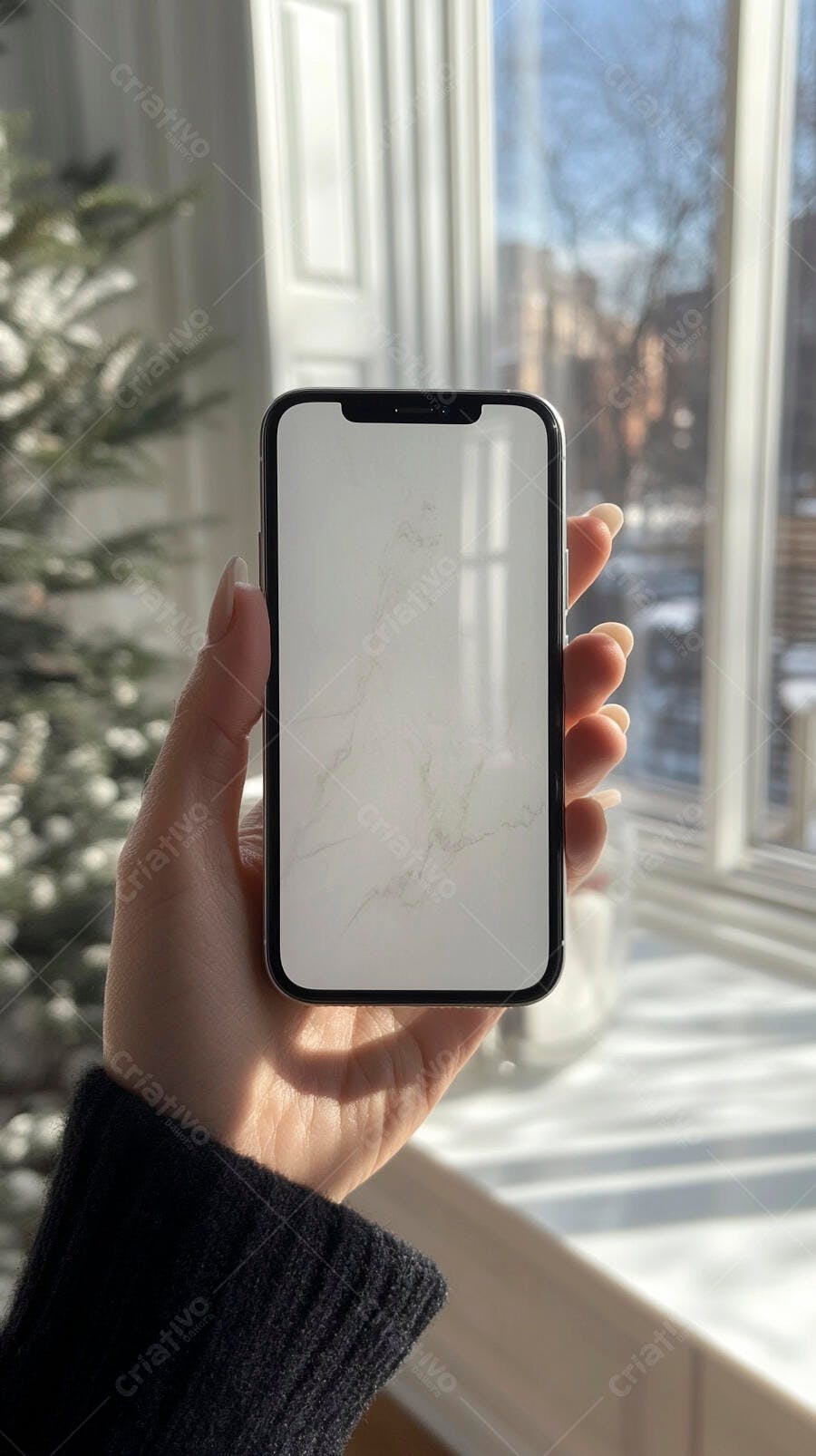 Mão feminina segurando smartphone tela mockup branca ao lado de janela ensolarada