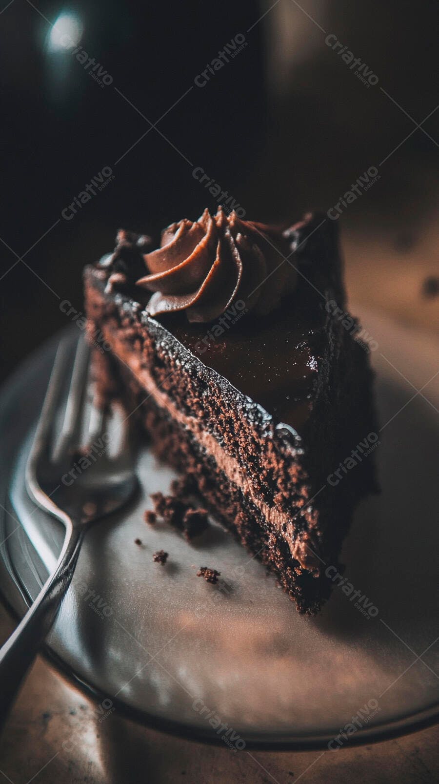 Fatia de bolo de chocolate com cobertura cremosa em prato escuro com garfo