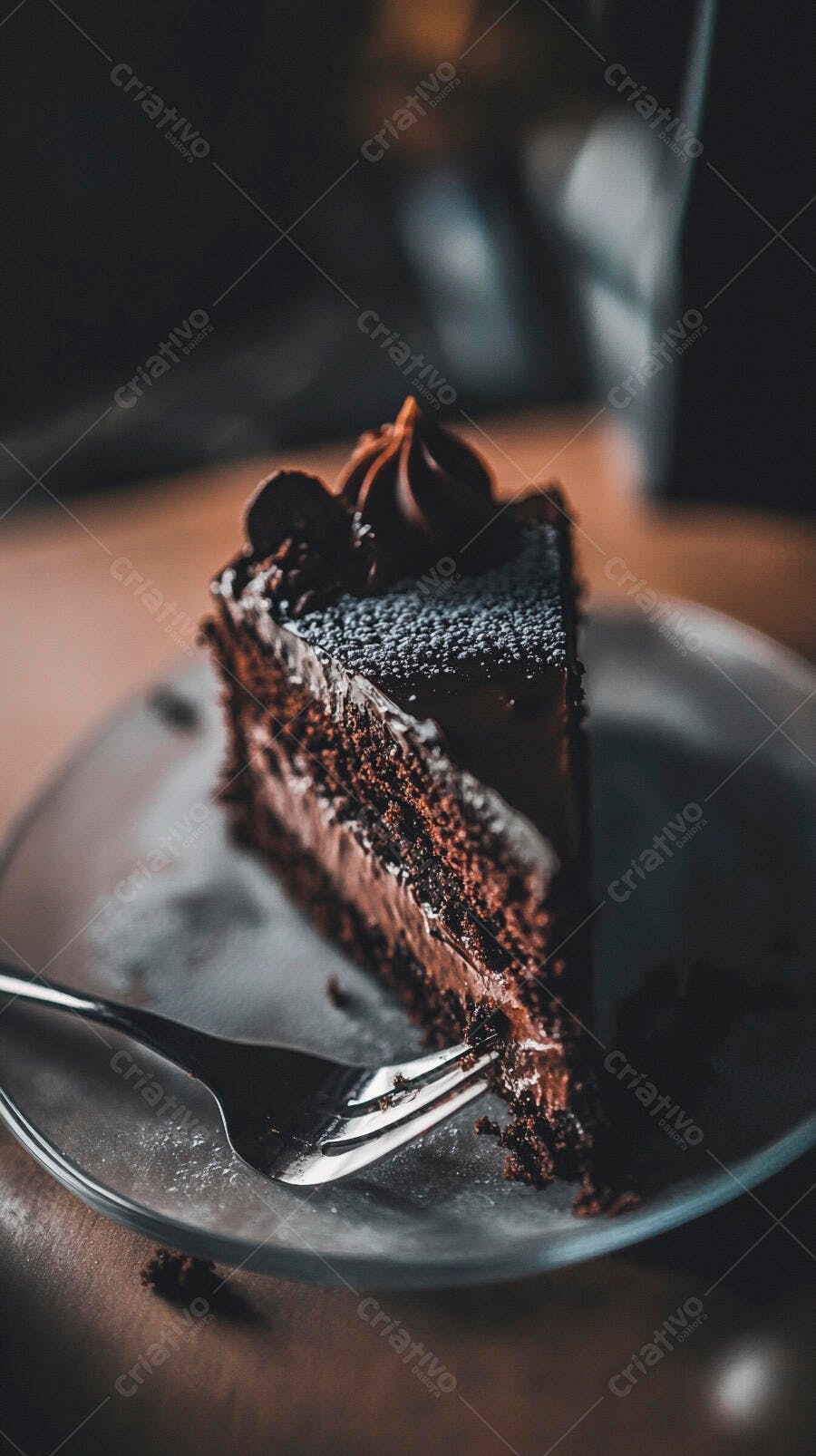 Fatia de bolo de chocolate escuro com cobertura e garfo em prato de vidro