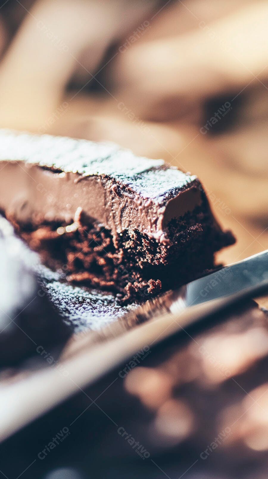 Bolo de chocolate denso com açúcar de confeiteiro e faca em mesa de madeira