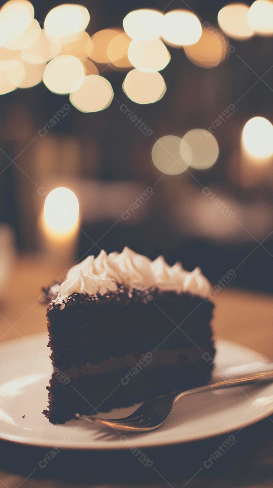 Fatia de bolo de chocolate com cobertura branca e garfo sobre luzes bokeh