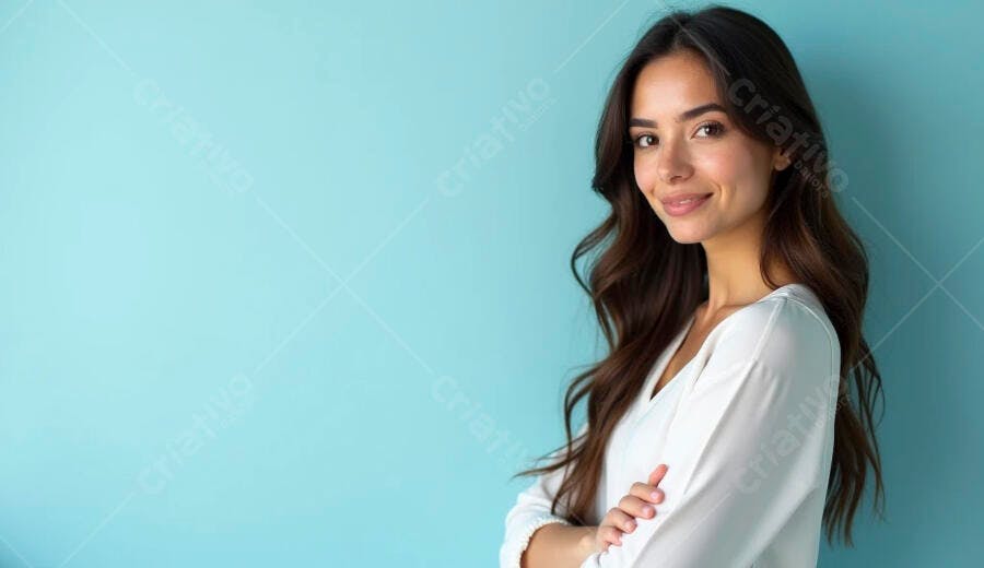 Mulher jovem de cabelos castanhos sorrindo de braços cruzados contra fundo azul claro