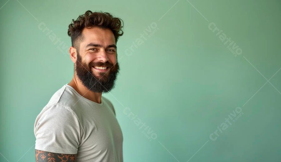 Homem barbudo sorrindo com camiseta cinza em fundo verde claro