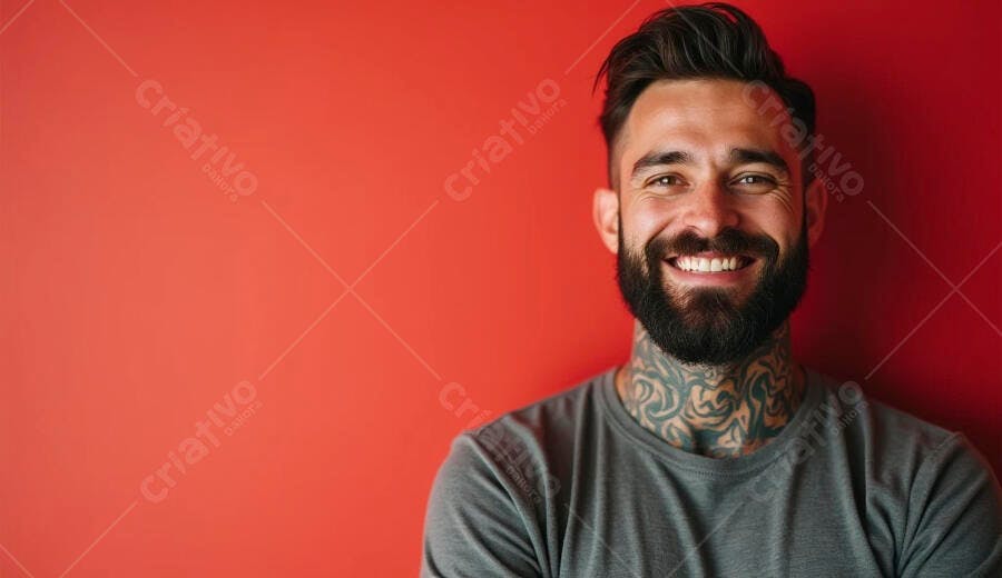 Homem caucasiano com barba e tatuagens no pescoço sorrindo em fundo vermelho