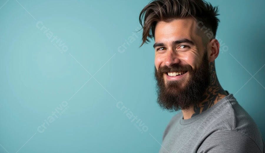 Homem barbudo sorrindo feliz com cabelo escuro e tatuagens em fundo azul turquesa