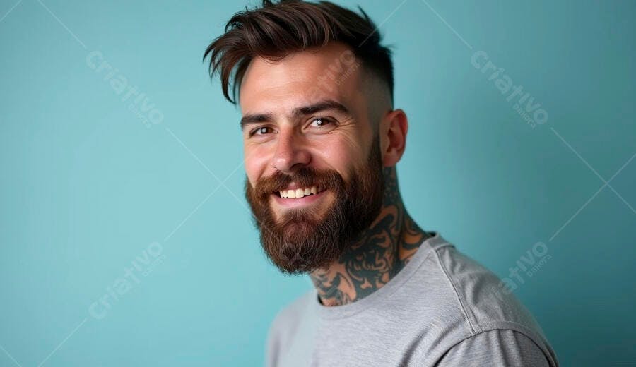 Homem barbudo jovem sorrindo com cabelo moderno e tatuagens em fundo azul claro