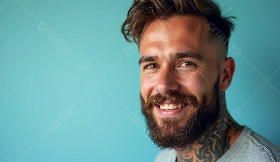 Homem barbudo tatuado sorrindo feliz em retrato de estúdio com fundo azul-claro