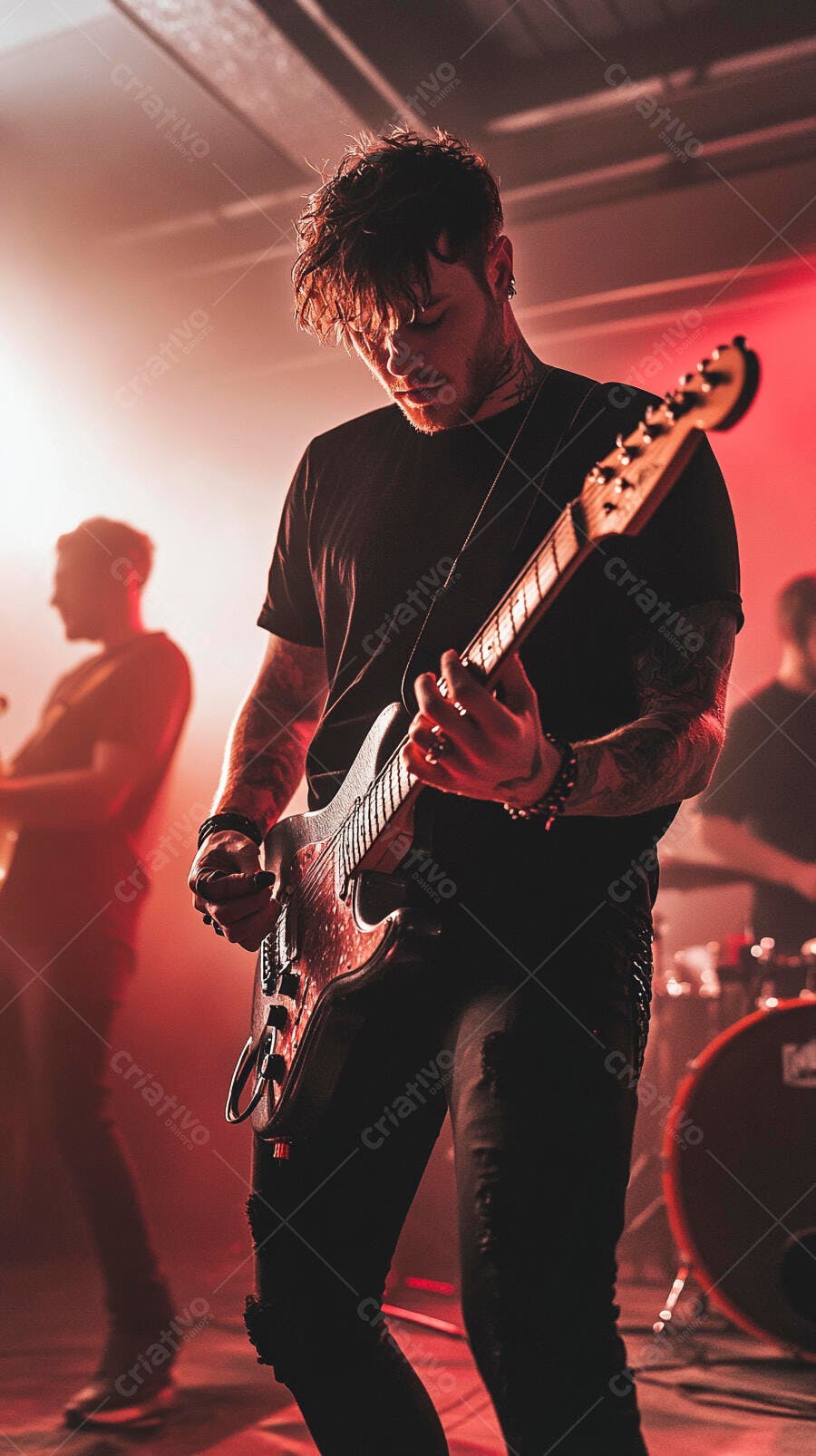 Homem branco tatuado tocando guitarra elétrica em show com luz vermelha