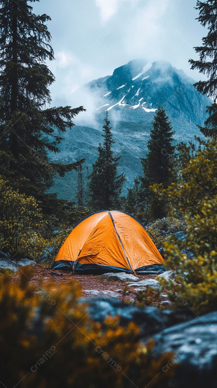 Barraca de camping laranja em floresta montanhosa com picos nevados e neblina