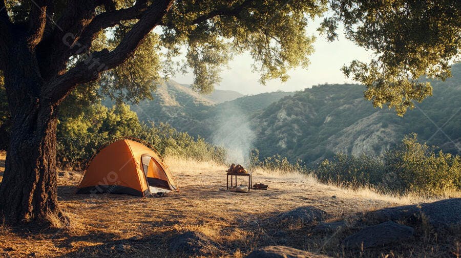 Tenda laranja em acampamento nas montanhas com fogueira e fumaça ao amanhecer